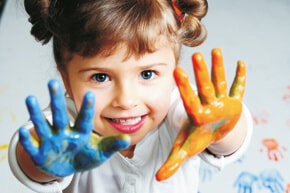Ein glückliches Kind zeigt seine mit Farbe verschmutzten Hände.